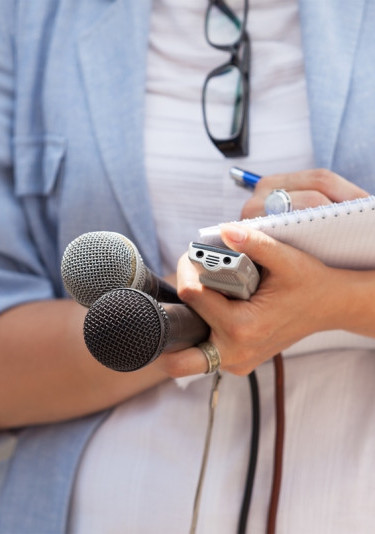 A journalist holding a microphone and taking notes on a notepad